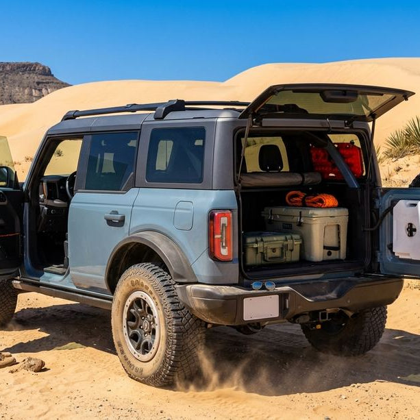 2024 Area 51 Ford Bronco Wildtrak 4-Door at a sand-dune playground at high noon with tailgate down and serious 4x4 recovery gear loaded — Hothead Headliner visible inside through the open driver door