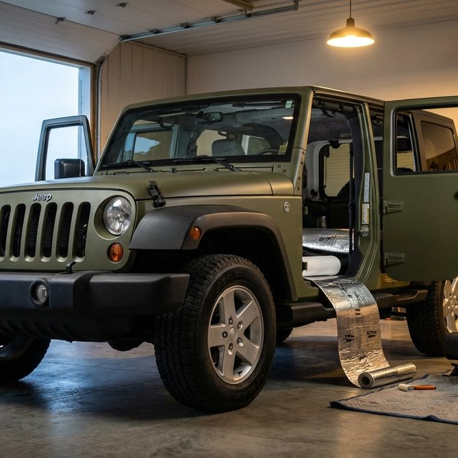 2012 Jeep Wrangler JK Unlimited in olive green inside an enthusiast workshop with all four doors open mid-install — Sound Assassin material rolled out in the rear and charcoal Hothead Headliner installed on the JK hard-top ceiling