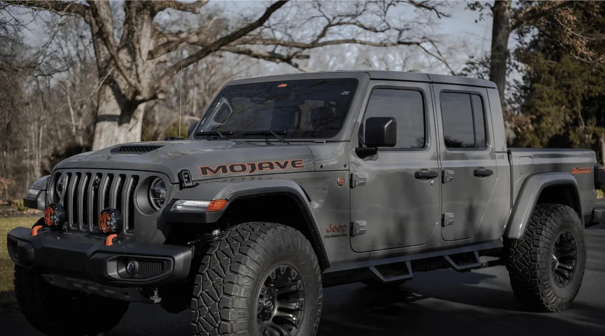 Gray Jeep Gladiator Mojave on black pavement with trees, showcasing Hothead Headliners for custom comfort and style